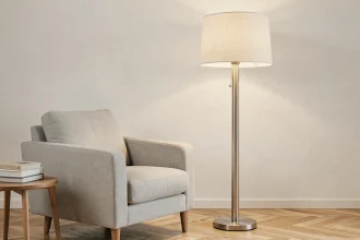 Lampe halogène sur pied en acier brossé avec abat-jour en tissu crème placée à côté d'un fauteuil gris dans un salon scandinave