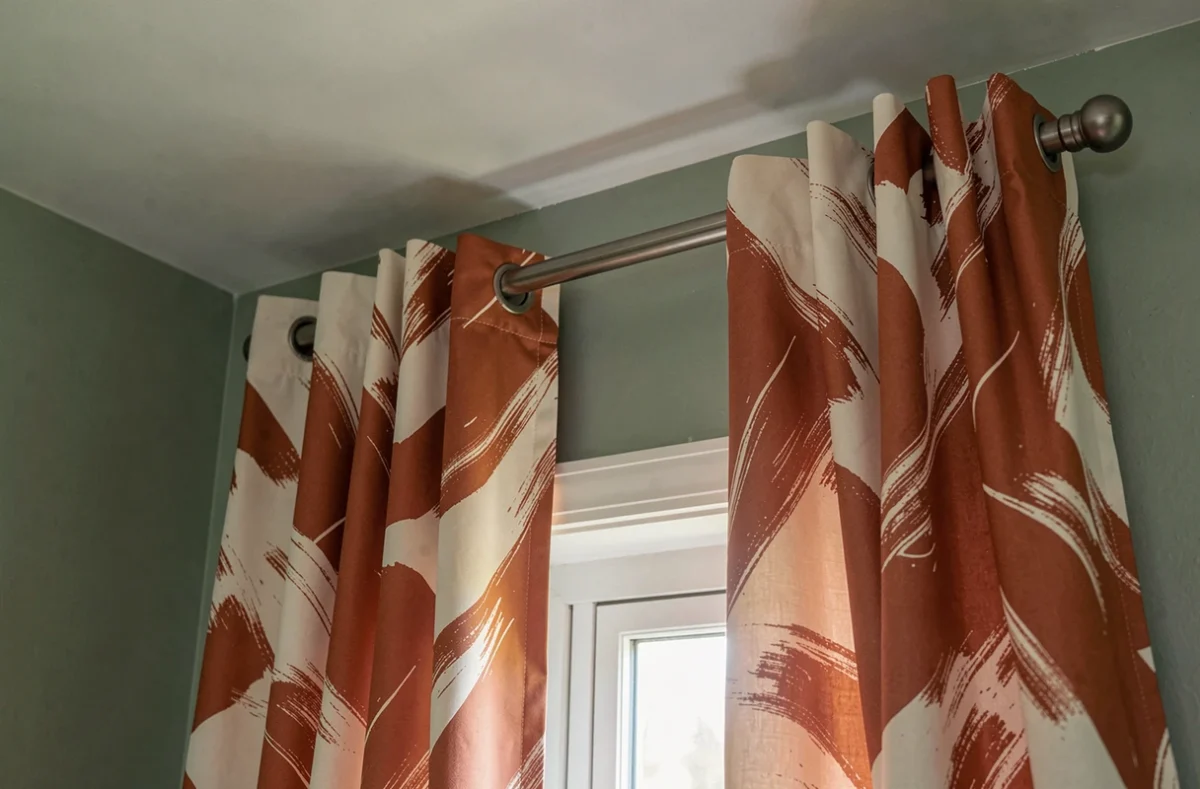 Détail de rideau occultant à motif abstrait posé trop bas sur la fenêtre, erreur de hauteur de tringle fréquente en décoration